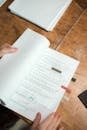 Person's hands holding script pages with handwritten notes on a wooden table.